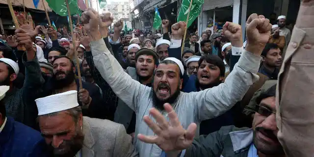 A large crowd of men, many wearing traditional white caps, raise their fists and chant passionately while holding green flags during a protest. The accompanying commentary suggests the post views the demonstration as evidence of widespread sentiment against the West, arguing that America in particular must acknowledge and publicly address the issue.