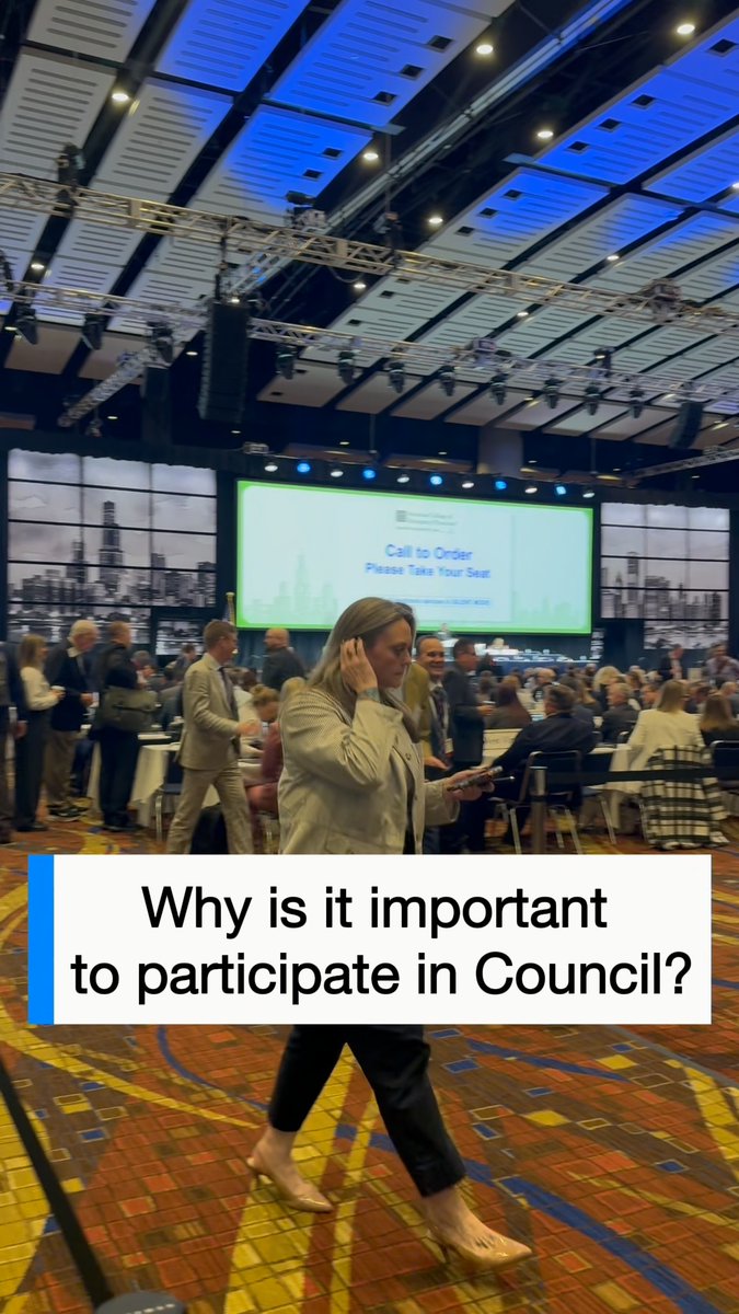 A woman in a beige blazer walks through a large conference ballroom during a city council meeting, with a presentation slide reading 'Call to Order - Please Take Your Seat' on the screen behind her.