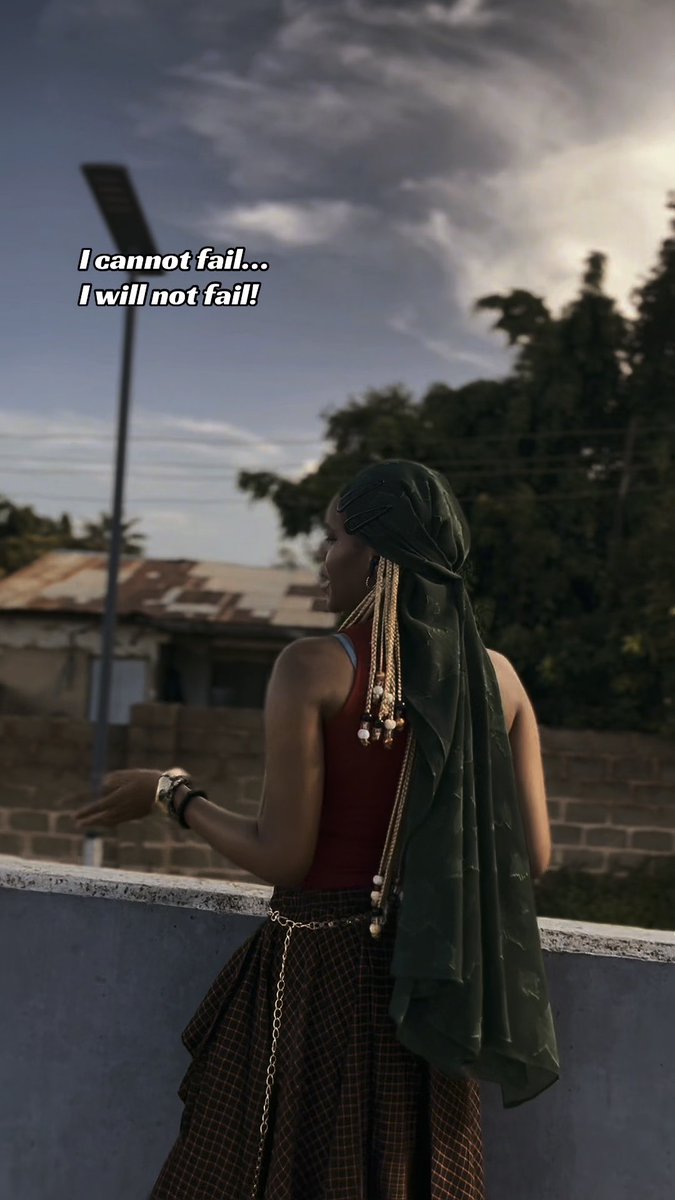 A woman in a green hijab and red top looks out over a low wall, with overlaid text reading 'I cannot fail... I will not fail!'