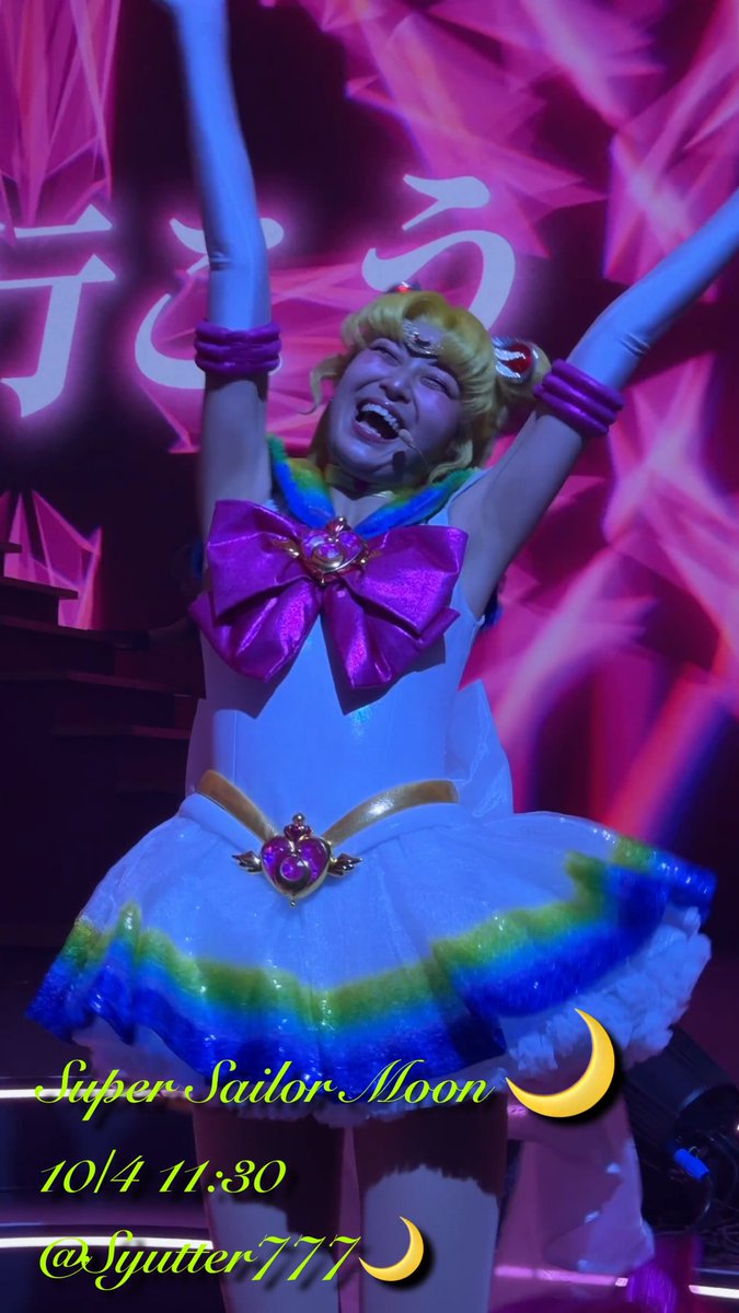 A performer in a Super Sailor Moon costume poses on stage with both arms raised in a triumphant pose, with text reading 'Super Sailor Moon, 10/4 11:30, @Syutter777' at the bottom.