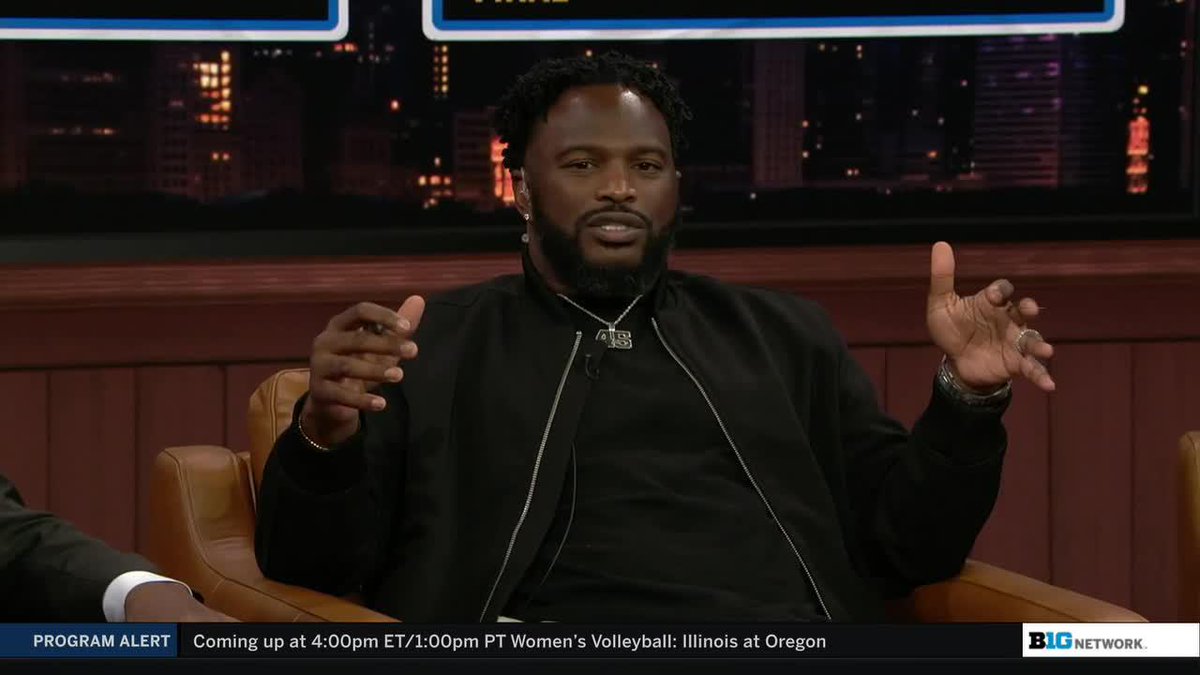 A man wearing a black jacket and "B1G" pendant gestures during an interview on the Big Ten Network, with a "PROGRAM ALERT" ticker at the bottom promoting upcoming Women's Volleyball coverage of Illinois at Oregon.