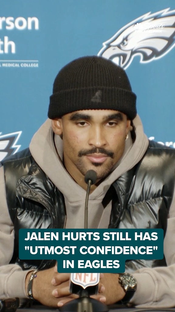 The image shows Jalen Hurts, quarterback of the Philadelphia Eagles, wearing a black beanie and black puffer vest at a press conference, with the Eagles logo and Jefferson Health branding visible in the background. A teal text overlay reads, "JALEN HURTS STILL HAS 'UTMOST CONFIDENCE' IN EAGLES," tying into the post's announcement that D-Jacc will appear on the WIP Midday Show to discuss Hurts' continued confidence in the team.
