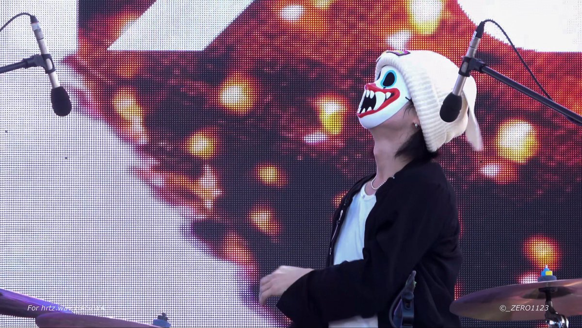 A performer wearing a white knit hat and a frightening mask with large blue eyes and sharp teeth stands on stage in front of microphones, with a watermark '© _ZERO1123'.