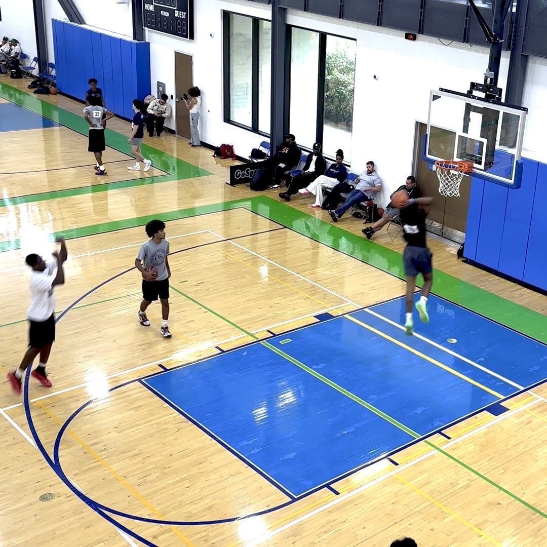 Players shoot hoops during an indoor basketball game on a court with blue and green accents.
