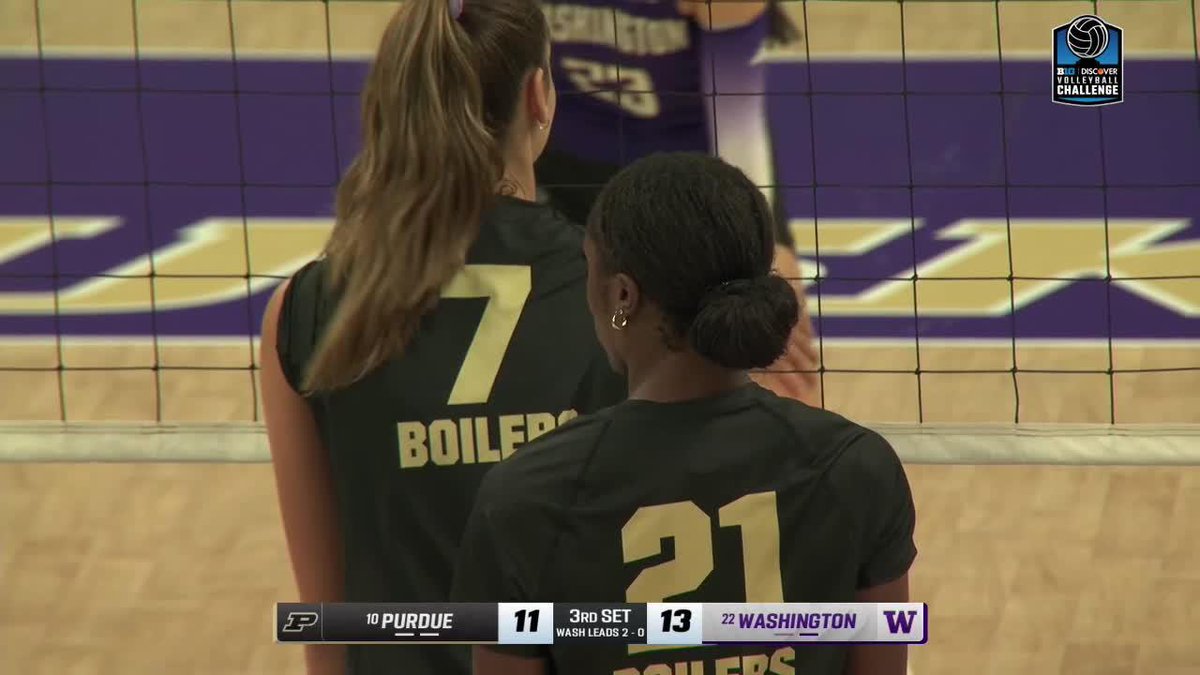 Two Purdue Boilermakers volleyball players (numbers 7 and 21) stand at the net during a match against Washington, with Washington leading 13-11 in the 3rd set.
