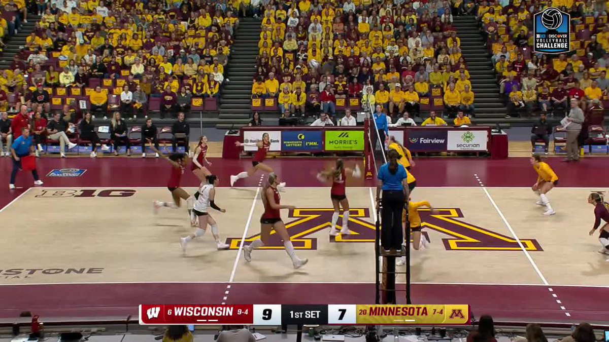 A volleyball game is in progress between Wisconsin and Minnesota. The on-screen scoreboard shows "WISCONSIN 9" and "MINNESOTA 7" in the "1ST SET".
