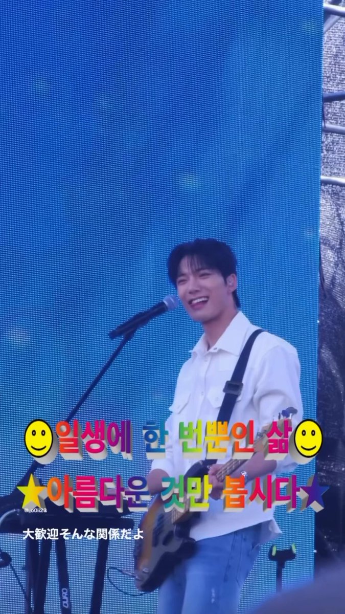 A smiling man in a white shirt plays a guitar on stage, with colorful overlaid Korean text reading '일생에 한 번뿐인 삶' and '아름다운 것만 봅시다' along with Japanese subtitles.