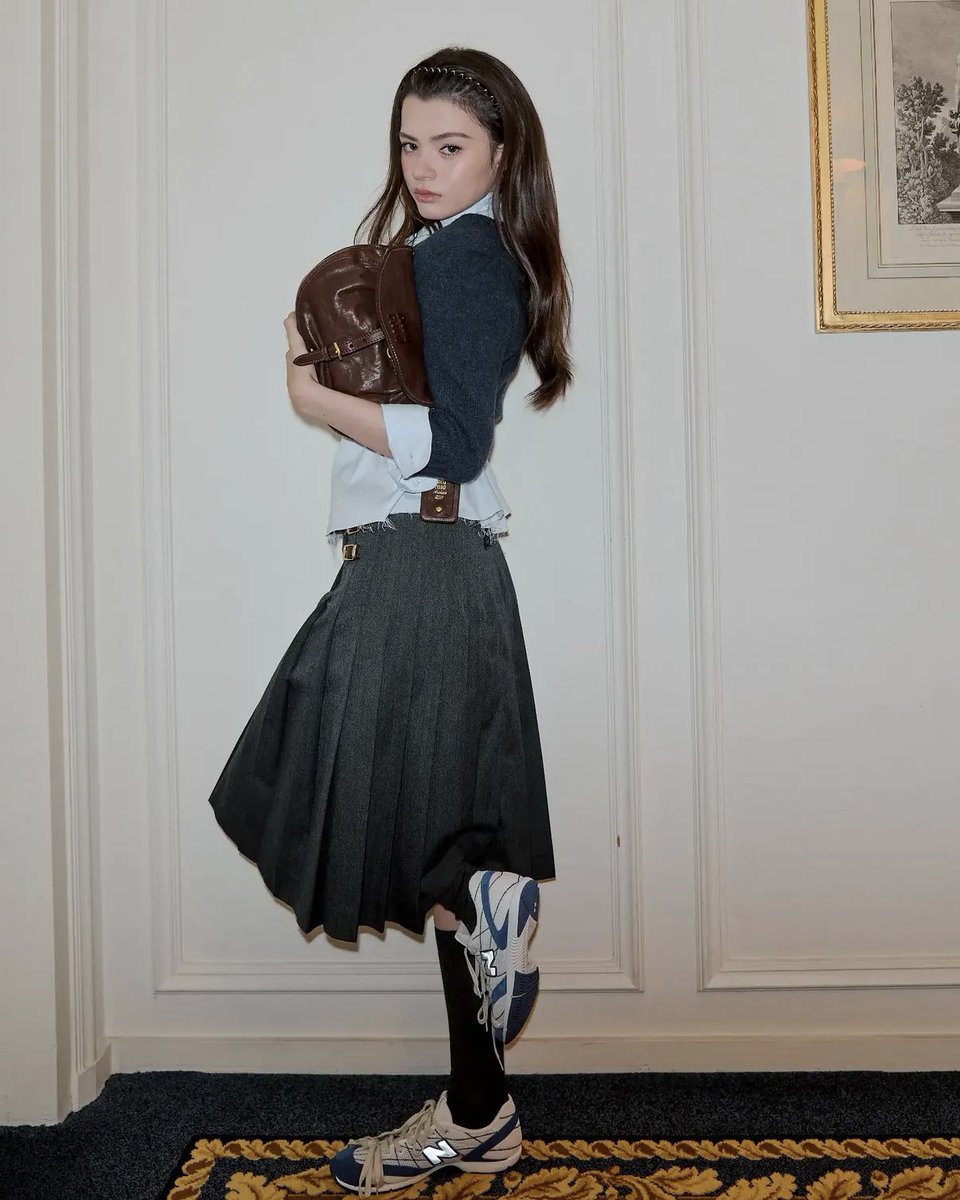 engagementbecky's tweet photo. 📸 | Pang Mak Thailand 

https://t.co/n0EabKKFVE

Irradiando charme e vivacidade de nível internacional! "Becky Rebecca" personifica o visual de uma jovem da alta sociedade tailandesa (*Khun Nu*) enquanto encanta Paris. Ela leva o fascínio da mulher tailandesa ao cenário global da moda ao marcar presença no desfile Primavera/Verão 2027 da Miu Miu, em Paris, França.

Becky Rebecca Patricia Armstrong exibe um conjunto chique da Miu Miu, composto por um cardigã escuro sobreposto com estilo a uma camisa azul. A camisa tem corte *cropped*, revelando um pouco da cintura e conferindo um toque de sensualidade delicada. Ela combina a peça com uma saia plissada cinza-escuro, detalhada com tiras duplas de couro e um cós cinza com a marca em destaque, enquanto uma tiara ricamente adornada completa seu visual refinado, típico da alta sociedade.

O *look* é finalizado com perfeição pela bolsa Miu Miu Rendez-vous em couro *nappa* marrom, que se destaca pela sua característica alça de couro trançado. Inspirada em um modelo de arquivo de 2011, a bolsa une harmoniosamente a herança clássica da marca ao estilo contemporâneo. Cada elemento se harmoniza para refletir com beleza tanto a identidade da grife quanto o charme tailandês da própria artista.

REBECCA X MIU MIU PFWSS27
#MiuMiuSS27xBecky
#beckysangels #BeckyArmstrong
#MiuMiuPFWxBecky #MiuMiuSS27
#MiuMiu #ParisFashionWeek
@MIUMIUofficial