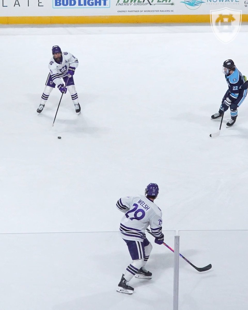 A hockey game scene showing a player wearing a white #29 'WELSH' jersey passing the puck to a teammate, with an opposing player in a light blue #22 jersey.
