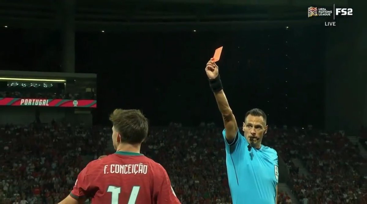 A referee in a light blue shirt raises a red card while facing a Portugal player named F. Conceição (number 11) during a UEFA Nations League match broadcast on FS2.