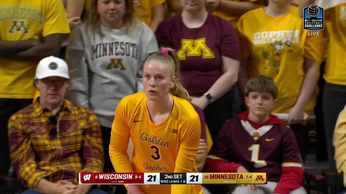 Minnesota Golden Gophers volleyball player #3 in a yellow jersey during a match, with the scoreboard showing Wisconsin and Minnesota tied 21-21 in the 2nd set, Wisconsin leading 1-0.