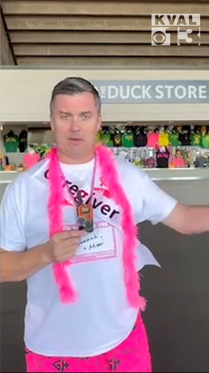 A news report screenshot from KVAL/CBS showing a man in a white t-shirt and pink feather boa at 'THE DUCK STORE', appearing to be a reporter or commentator.