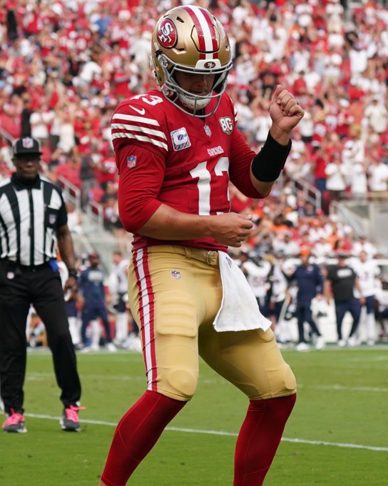 San Francisco 49ers quarterback #13, wearing the team's red and gold uniform with a captain's "C" patch and the "85" season anniversary logo, celebrates with a fist pump on the field. The image captures a celebratory moment, fitting the post noting that Brock Purdy is among the league leaders with 11 touchdown passes through four weeks of play.