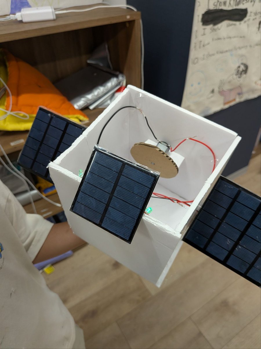 cgk_ja's tweet photo. 子どもの『人工衛星が気になる』を、調べ学習だけで終わらせない。

『人工衛星はどう動き、どう電気を作って使うのだろう？』。アフタースクール(対象G1–9)のミニプロジェクトで、一人の生徒が人工衛星をテーマに選びました。

調べるだけで終わらず、本物の太陽光パネルでLEDを光らせる模型を制作。さらに、モーターと回転する円盤を使った太陽光駆動のジャイロスコープにも取り組み、衛星の向きを保つ仕組みを探りました。

長期のPBLとは別に、ミニプロジェクトでは生徒が調べたいこと、調べ方、成果の表し方を選びます。発表の機会も設け、興味を調査、制作、説明へとつなげています。

模型は、本物の衛星そのものではありません。それでも、目に見えにくい仕組みを、自分の手で扱える形にして考えることができます。興味を出発点に、調べた知識を制作に使い、何を表している模型なのかを説明する。この往復を大切にしています。

CGK Times9月号より:
https://t.co/y9XWEOT3NV