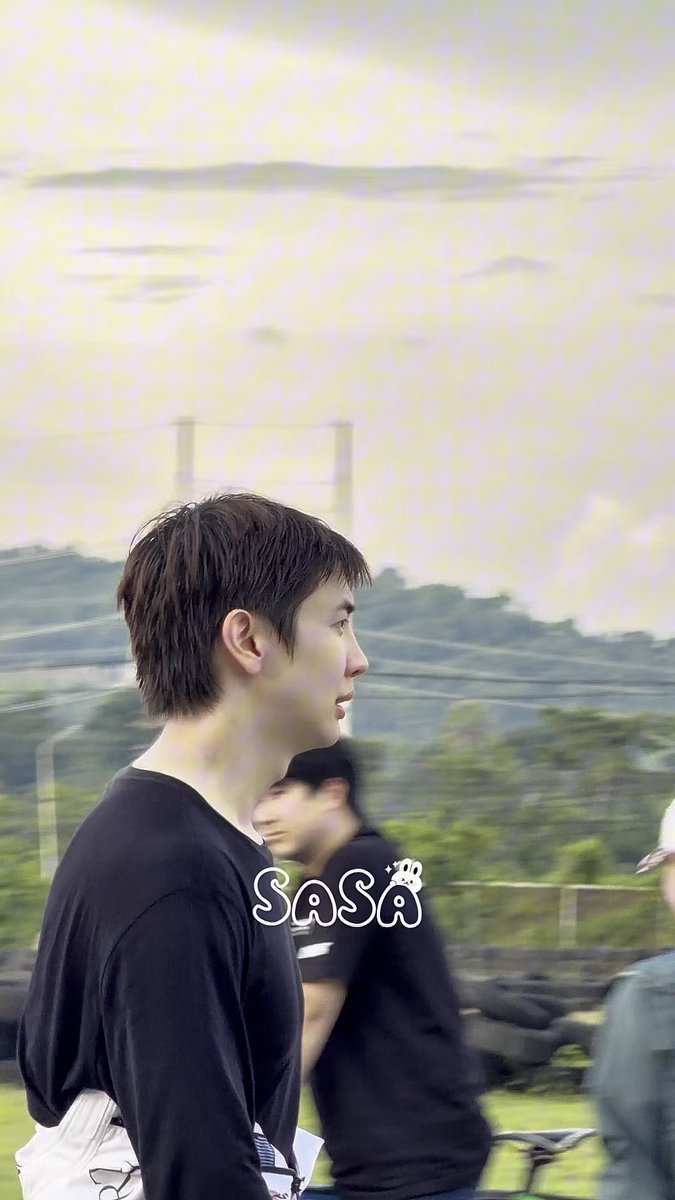 A side profile of a young man with brown hair wearing a black long-sleeved shirt, standing outdoors with a watermark 'Sasa' featuring a small bear logo.