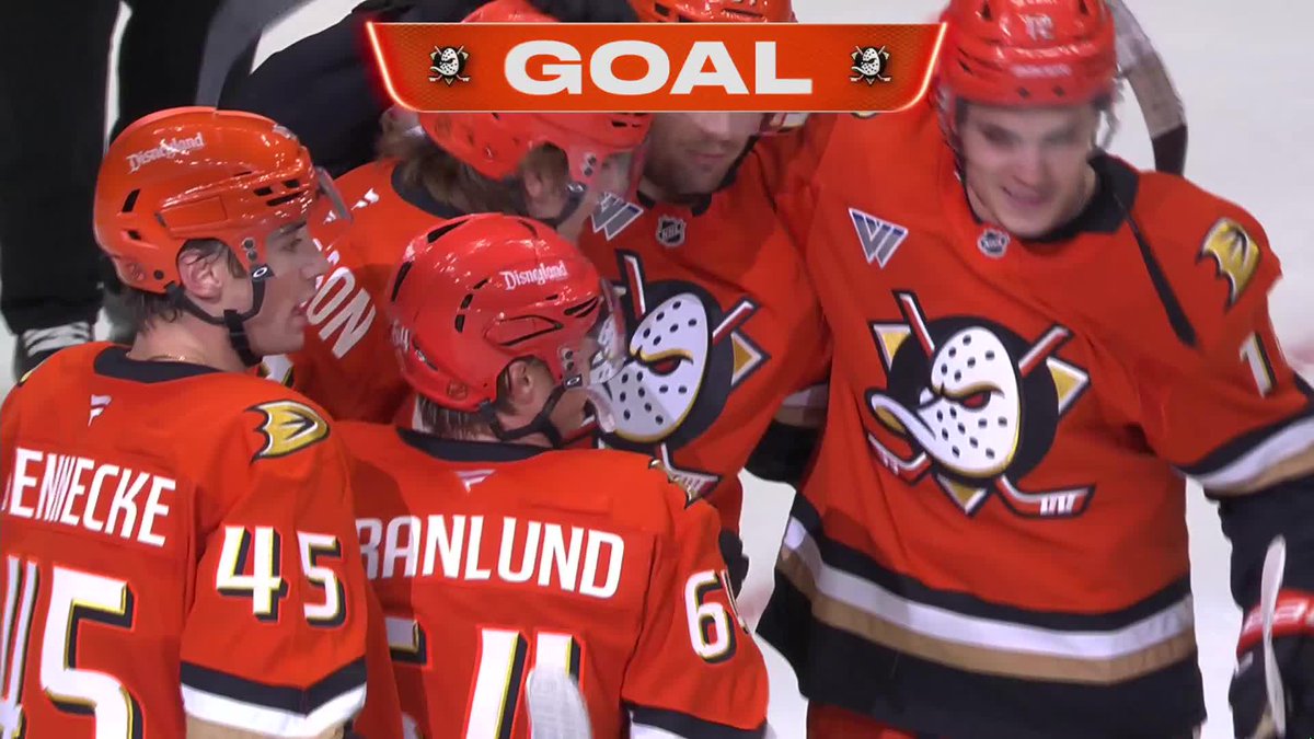 Anaheim Ducks players, including #45 Sennecke and #6 Granlund, celebrate together in their bright orange "Disneyland" helmets and jerseys after a goal, with a "GOAL" banner displayed above them. The image perfectly captures Granlund's triumphant moment as captain, showcasing the team's excitement following his overtime game-winning goal in his first home game wearing the C.