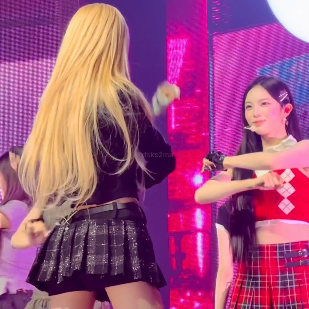 A concert photo showing a blonde performer dancing on stage while a smiling woman in a red and white outfit looks on.