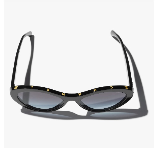 A pair of black Chanel sunglasses with the 'CHANEL' logo spelled out in gold lettering across the bridge, photographed against a white background.