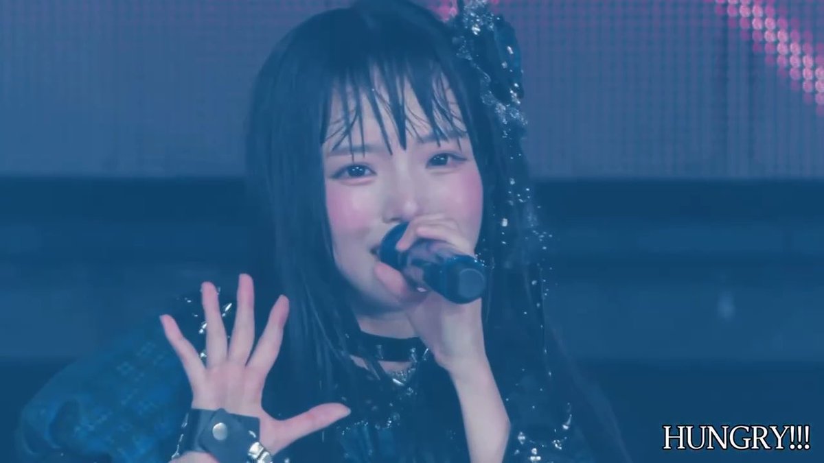 A close-up of a Japanese performer singing into a microphone on stage, wearing a black outfit with a hair accessory, with the text "HUNGRY!!!" displayed in the bottom right corner.