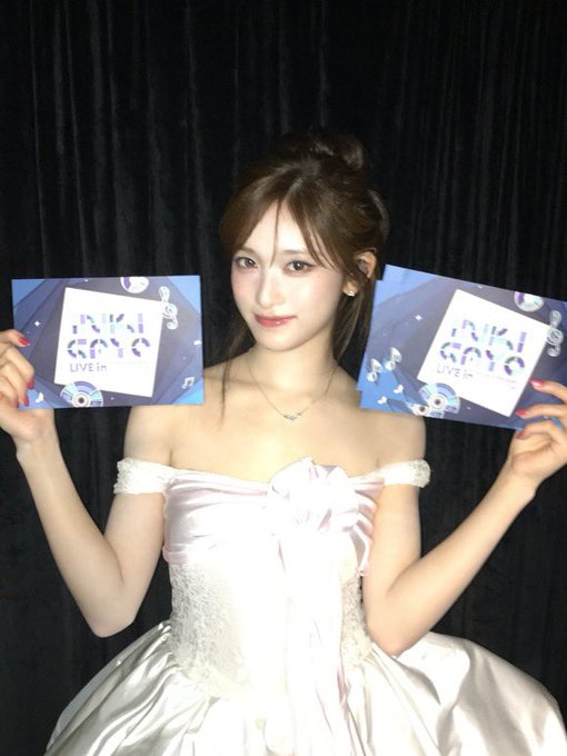 A young woman in a pink off-shoulder dress holds up two signs that read "IVY GAYO LIVE in".