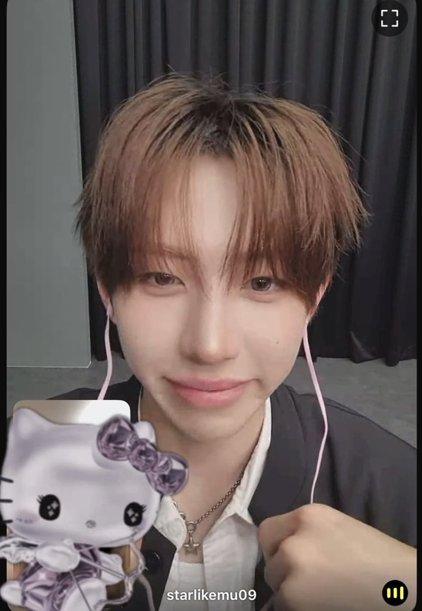 A close-up of a young man with brown hair wearing pink earphones, with a Hello Kitty figurine in a purple dress superimposed on the left, and the username "starlikemu09" displayed at the bottom.