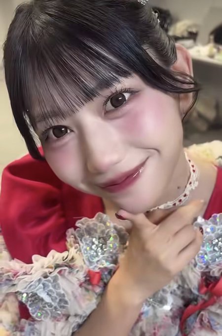 A close-up selfie of a young woman with pink blush and glossy lips wearing a sparkly red and pink outfit with a floral choker.