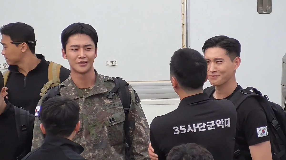 A group of Korean men, including one in military camouflage uniform and others in black polo shirts, with "35사단군악대" (35th Division Military Band) visible on one shirt and "대한민국 육군" (Republic of Korea Army) on the uniform.