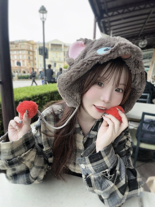 A young woman wearing a fuzzy bear-themed hat and a black-and-white plaid shirt poses with two strawberries.