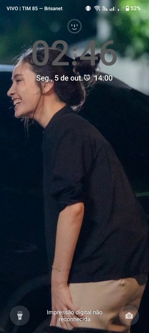 A phone lock screen showing the time 02:46 on Tuesday, October 5th, with a wallpaper of a smiling woman in a black shirt leaning out of a vehicle.