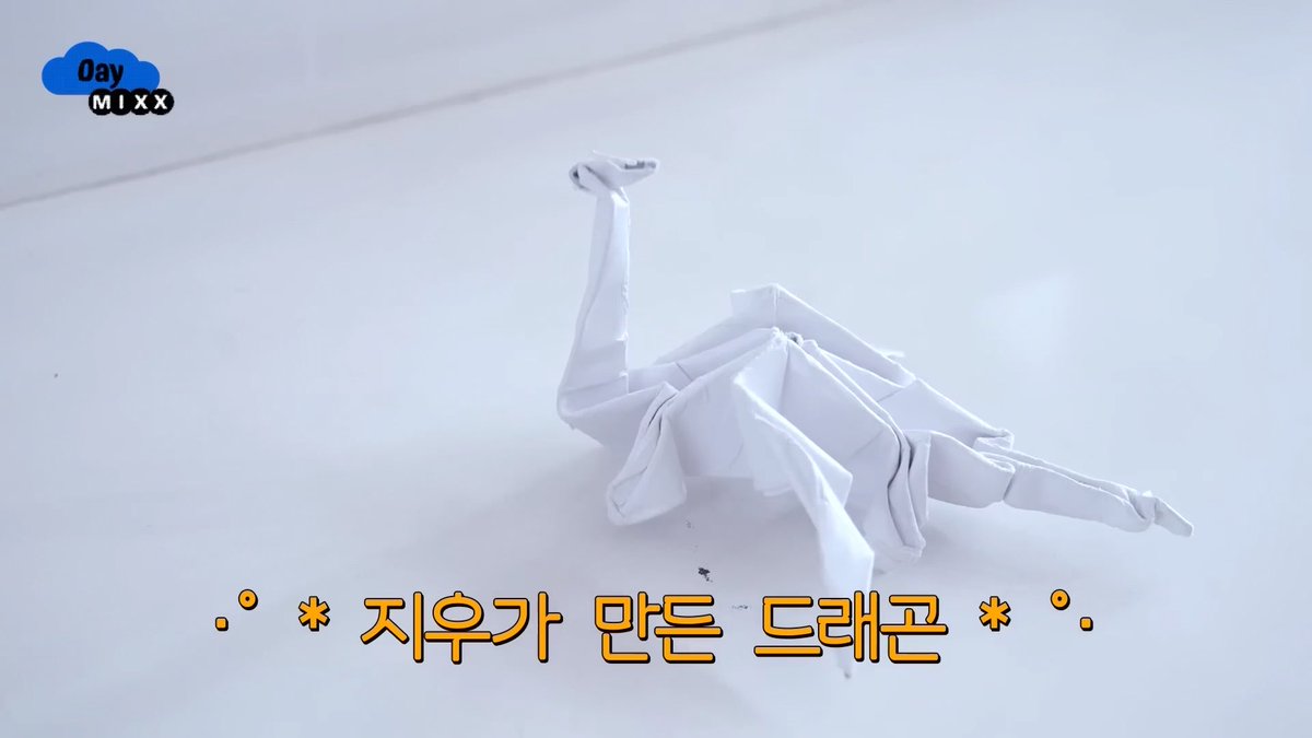 A white origami dragon sculpture displayed on a white surface, with a 'Day MIXX' logo in the corner and Korean text '지우가 만든 드래곤' (Dragon made by Jiwoo) at the bottom.