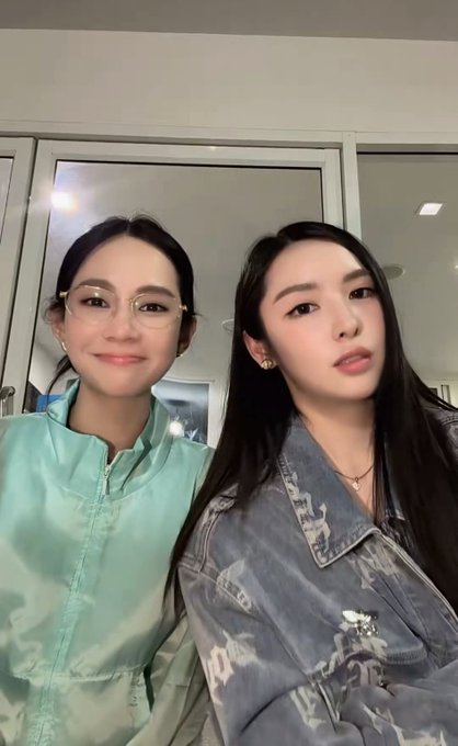 A selfie of two young women posing together; the one on the left wears glasses and a light blue jacket, while the one on the right wears a denim jacket.