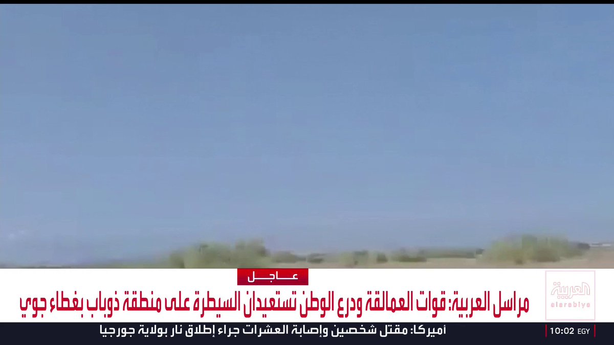 The screenshot shows a blurred desert landscape beneath a clear blue sky, with an Al Arabiya news banner at the bottom displaying an "عاجل" (breaking news) headline in Arabic stating: "مراسل العربية: قوات العمالقة ودروع الوطن تستعيدان السيطرة على منطقة ذوباب بغطاء جوي," with the location tag "أبواباب.. مقتل شخصين وإصابة العشرات جراء إطلاق نار بولاية جورجيا" and "10:02 EGY" timestamp.