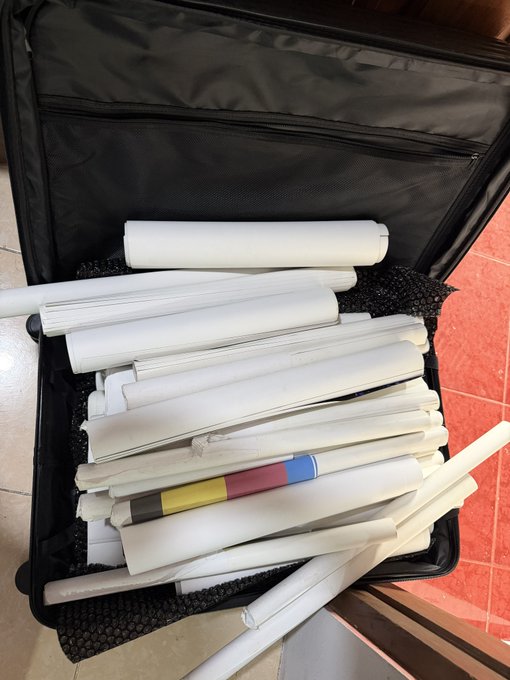 An open black suitcase packed with numerous rolled-up papers, posters, or tubes.