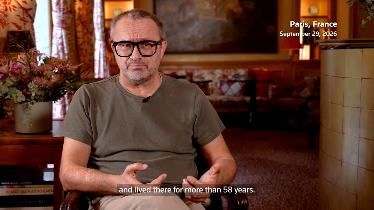 A bespectacled, gray-haired man in an olive t-shirt sits speaking in an ornately decorated room, with on-screen text identifying the location as "Paris, France" and dated "September 29, 2026," along with subtitles reading "and lived there for more than 58 years." The image relates to the accompanying post as it appears to be an interview setting with exiled Russian filmmaker Andrey Zvyagintsev, who is discussed in the context of his film "Minotaur" addressing Putin's war in Ukraine.