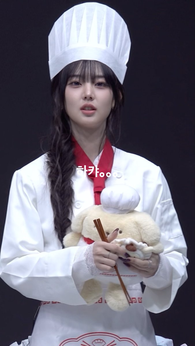 A young woman dressed as a chef in a white uniform and tall chef's hat, holding a plush sheep toy and wooden chopsticks, with Korean text '=카' overlaid on the image.