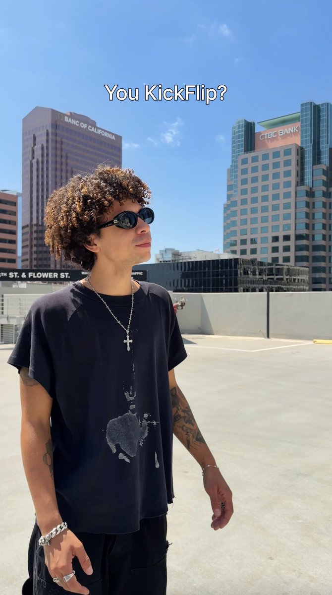 A young man with curly hair, sunglasses, and a black graphic t-shirt stands on a rooftop with the text 'You KickFlip?' overlaid; skyscrapers including 'BANK OF CALIFORNIA' and 'CTBC BANK' are visible in the background.