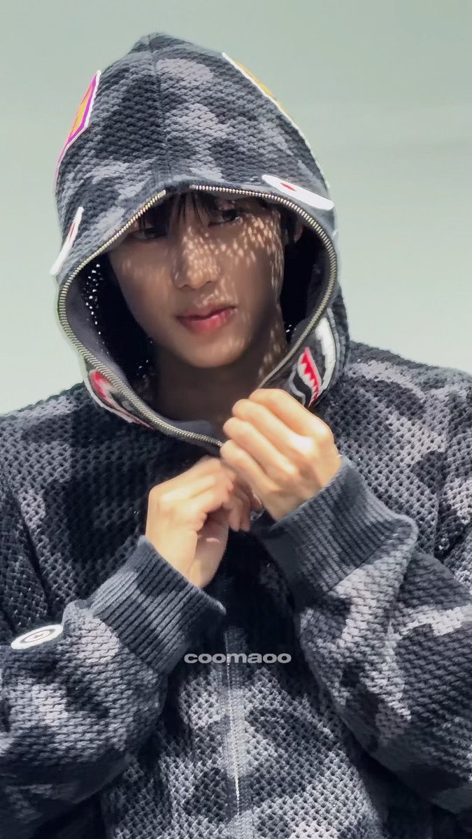 A young man wearing a grey camouflage hoodie pulled over his head, with patterned shadows cast on his skin and the text 'coomaoo' at the bottom.