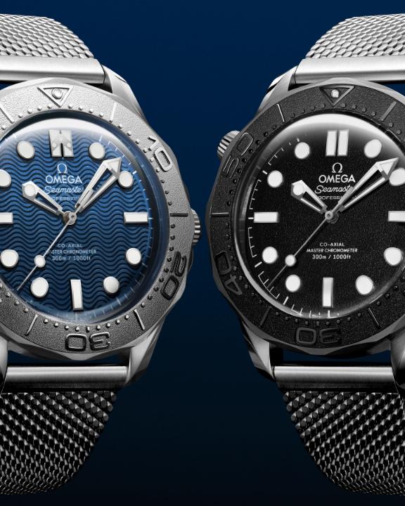 Two Omega Seamaster Diver 300M watches are displayed side by side—one featuring a blue wave-patterned dial and the other with a black dial—both bearing the "OMEGA Seamaster Co-Axial Master Chronometer 300m/1000ft" inscription, representing the "James Bond" and "Spectre" themed timepieces from OMEGA's Timeless Adversaries collection.