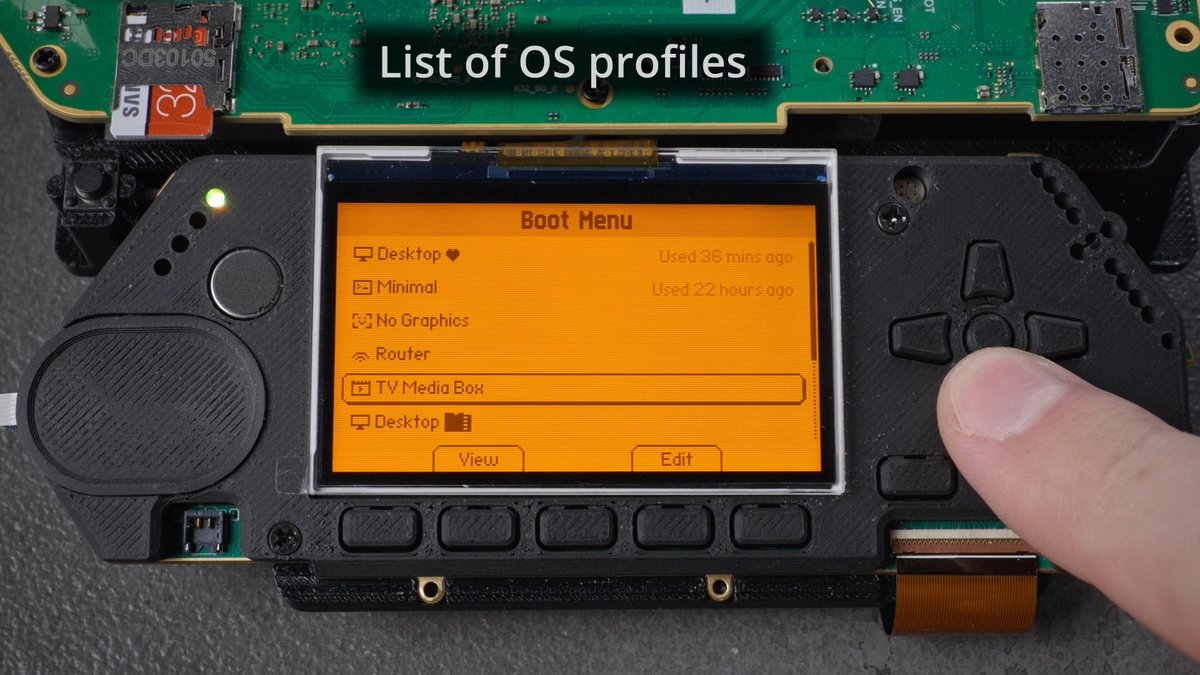The image shows a Flipper One device displaying its new boot menu on an orange screen, with a list of OS profiles including "Desktop ♥," "Minimal," "No Graphics," "Router," "TV Media Box," and "Desktop 🗂️," with the "TV Media Box" option currently highlighted. A user's thumb is pressing the directional pad on the right side of the device to navigate the menu, illustrating the intuitive interface mentioned in the post that allows users to manage and select OS profiles for booting.