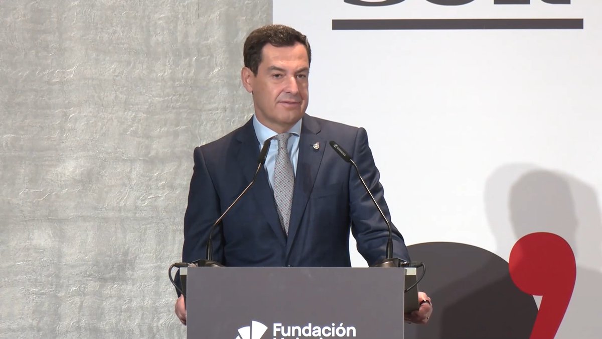 A man in a dark suit stands at a podium with the "Fundación" logo, appearing to be delivering a speech at a formal event. The image, paired with criticism of Sánchez's government for underinvesting in Andalusian commuter rail, suggests the speaker is likely a regional political figure from Andalucía addressing infrastructure neglect.