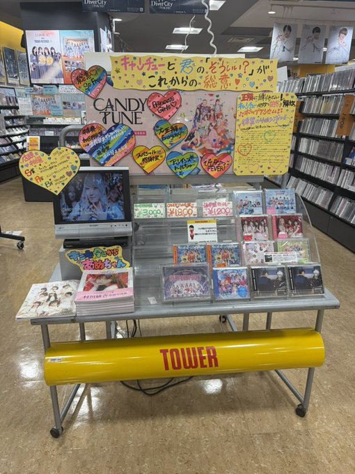 A Tower Records promotional display in a store features CDs and merchandise for the Japanese idol group Candytune, with colorful heart-shaped signs and a small TV screen showing performance footage.