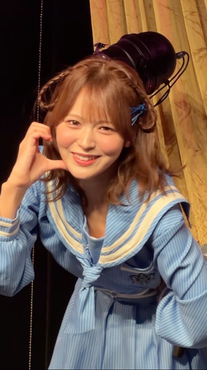 A cheerful young woman with braided pigtails smiles and makes a heart shape with her hand, wearing a light blue striped sailor-style outfit, in what appears to be a backstage photo posted with the caption "ほんとうにすきです #江角怜音" (I really love it/suit #ReotoEsumi), suggesting the image relates to her support or affection for the performer or character Reoto Esumi.