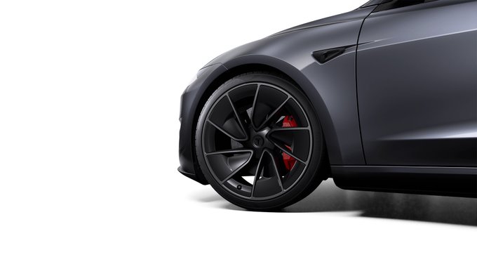 A close-up view of a dark gray Tesla vehicle showcasing its black alloy wheel with red brake calipers visible through the spokes.