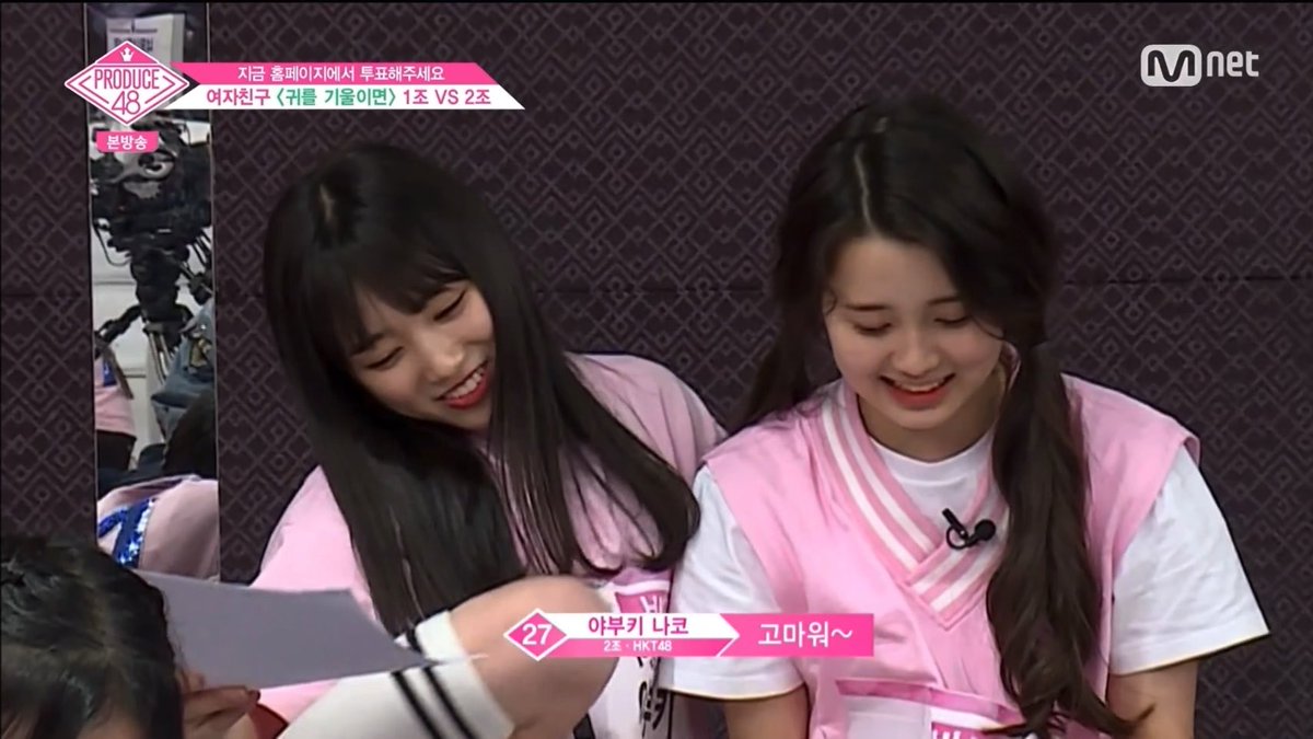 The screenshot from the Mnet show "Produce 48" features contestants Azabu Kibuki (#27, 2nd gen, HKT48) and Ko Miu in matching pink outfits, smiling warmly during a 1-vs-1 vocal battle segment ("여자친구 <귀를 기울이면> 1조 VS 2조"). The wholesome, emotionally charged moment aligns perfectly with the captioner's confession about being emotionally moved—even to tears—by idol survival show footage, capturing exactly the kind of heartwarming scene that prompts such reactions from devoted viewers.