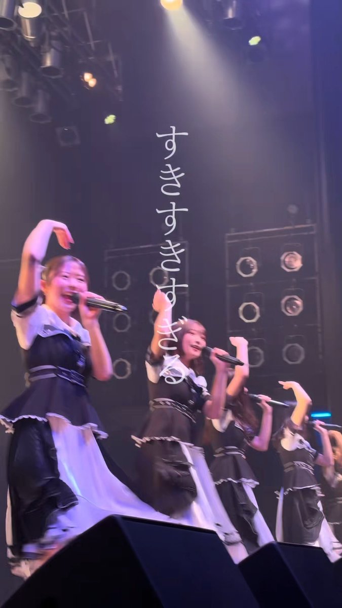 A group of young women in matching black and white outfits perform on stage with microphones, with Japanese text overlaid that reads "さよならさんは本当に" (Goodbye-san is really...).