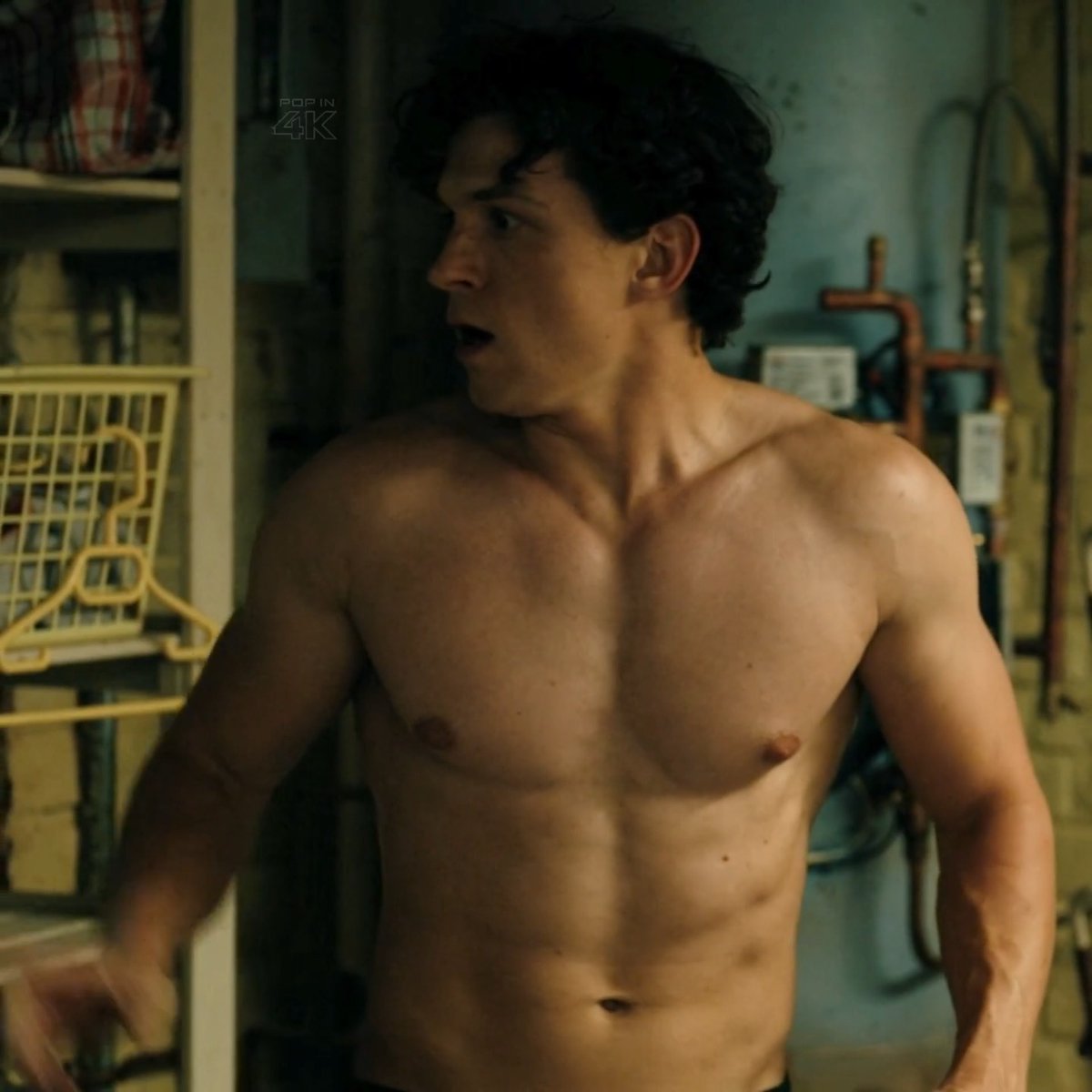 A shirtless young man with dark curly hair stands in what appears to be a basement or utility room with exposed pipes and shelves. The scene has a cinematic quality with a 'POP IN 4K' watermark visible in the upper left.
