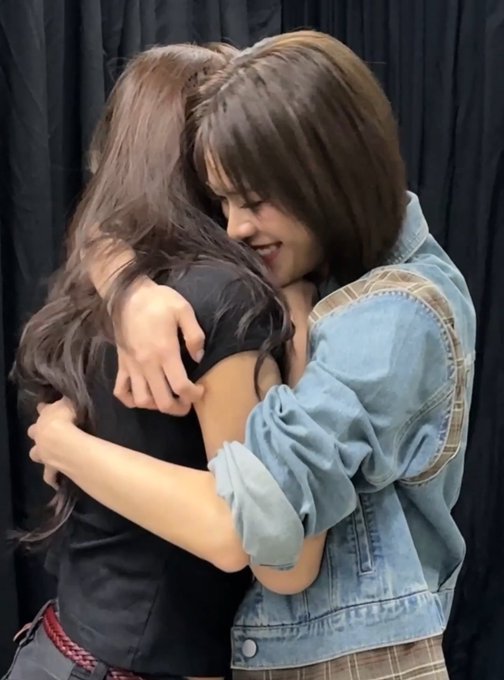 Two women hugging, one with long dark hair and the other with a bob haircut wearing a denim jacket.