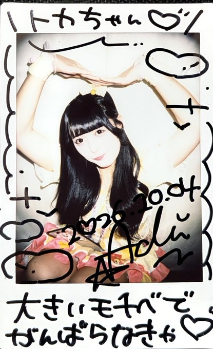 A Polaroid-style photo of a young woman with long dark hair posing with her arms raised above her head, surrounded by handwritten Japanese text and doodles including hearts.