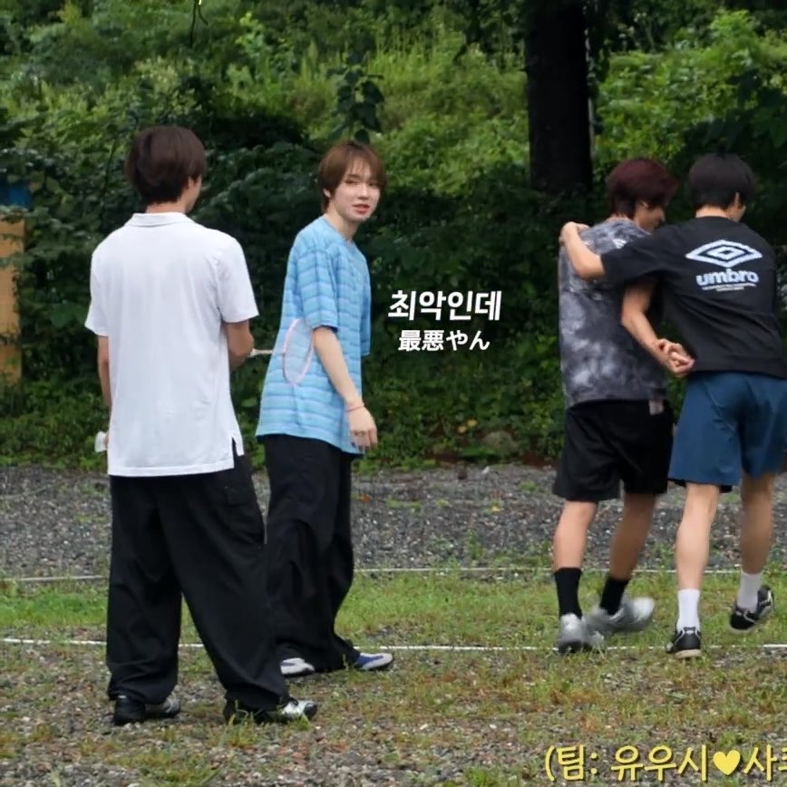 Four young men stand on a gravel and grass outdoor court, with two on the right playfully grappling each other, one wearing an Umbro shirt. The Korean/Japanese on-screen text reads "최악인데 / 最悪やん" ("it IS the worst"), capturing their reaction at discovering they are evenly matched in skill and thus stuck together as teammates, humorously echoing the post's comparison to the chaotic duo from Badminton Cheeseballs.