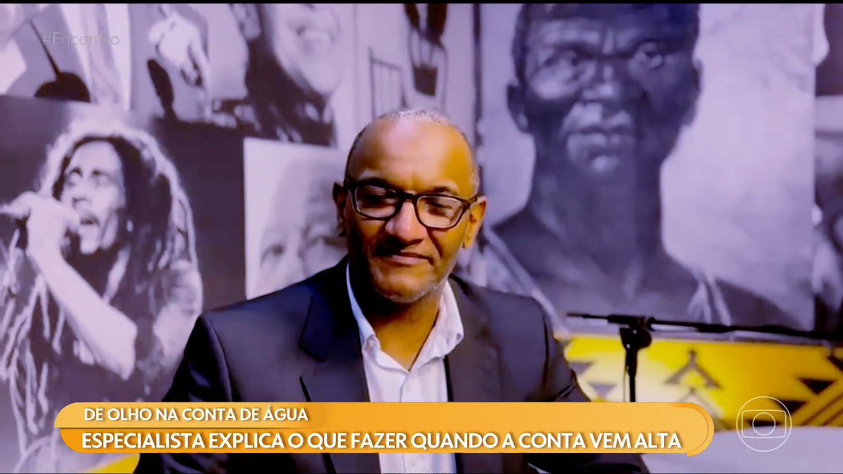 A man wearing glasses and a dark suit sits in front of a backdrop featuring black and white photos, with Portuguese text reading 'DE OLHO NA CONTA DE ÁGUA' and 'ESPECIALISTA EXPLICA O QUE FAZER QUANDO A CONTA VEM ALTA' displayed at the bottom.